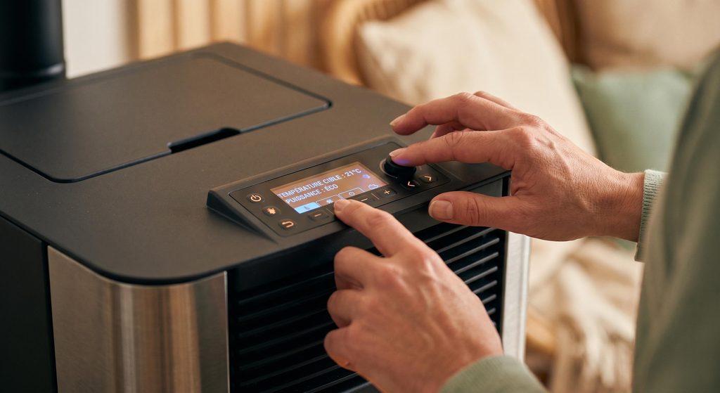 Main réglant le thermostat digital d'un poêle à granulés, économies d'énergie