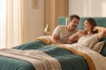 Couple souriant se réveillant sur un grand matelas confortable, lumière du matin douce
