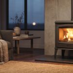 Poêle à bois Godin Châtel noir mat dans un salon cosy, flammes visibles à travers la vitre, ambiance chaleureuse