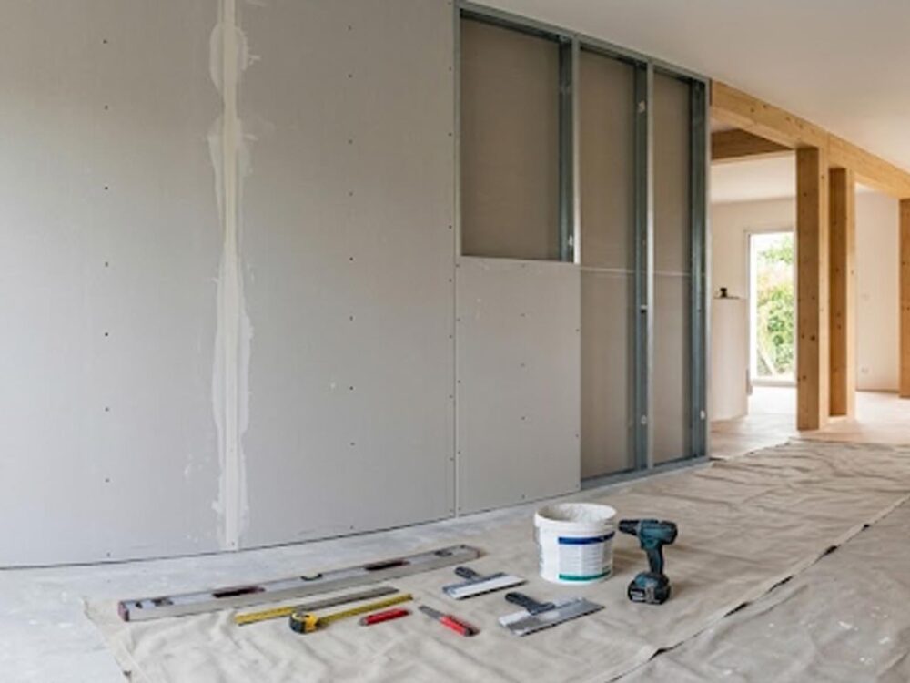 Plaques de plâtre en cours de pose dans un salon moderne en rénovation, montrant les étapes du cloisonnement.